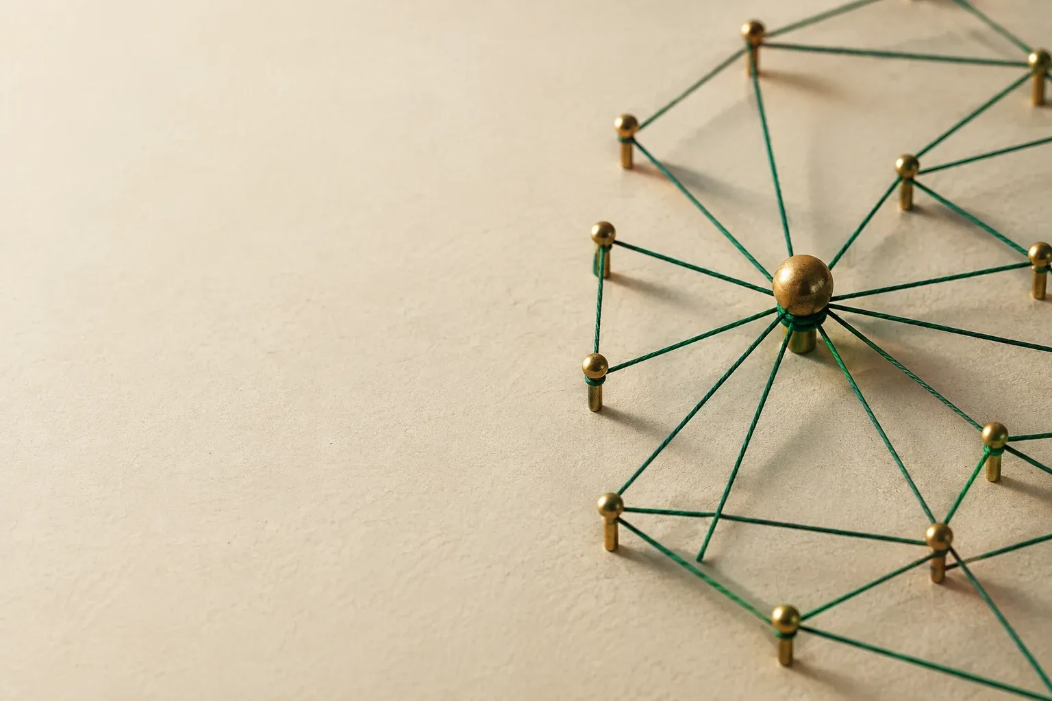 A web of thin green cord stretched between brass pins on an ivory corkboard, one central pin larger than the rest